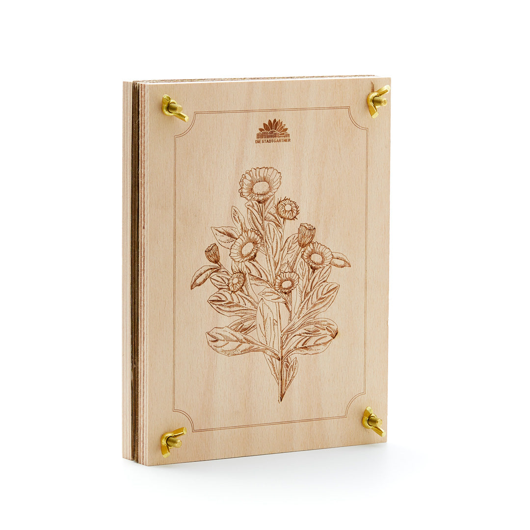 Libro de madera con patrón de grabado floral y esquinas de metal dorado, sobre un fondo blanco.