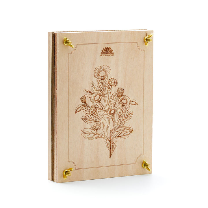 Libro de madera con patrón de grabado floral y esquinas de metal dorado, sobre un fondo blanco.