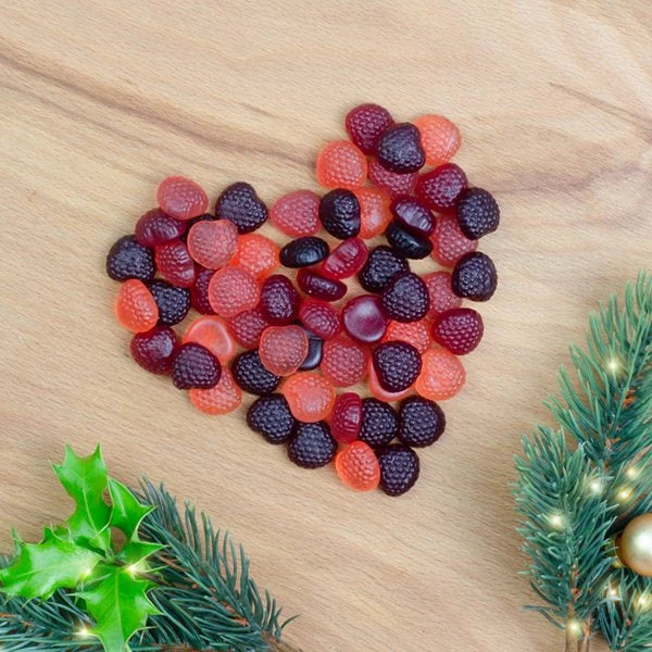Ositos de goma con forma de corazón sobre un fondo de madera con una rama de abeto y una hoja de acebo.