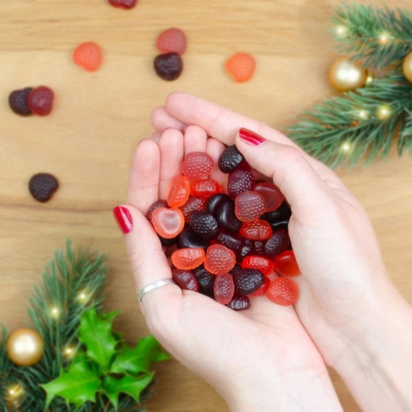 Manos con esmalte de uñas rojo sosteniendo ositos de goma, decoraciones invernales en el fondo.