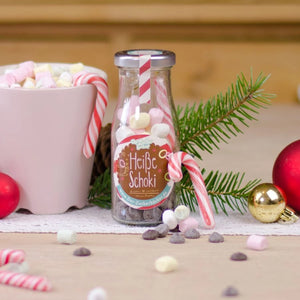 Botella etiquetada "Chocolate caliente" junto a adornos navideños y una taza de malvaviscos.