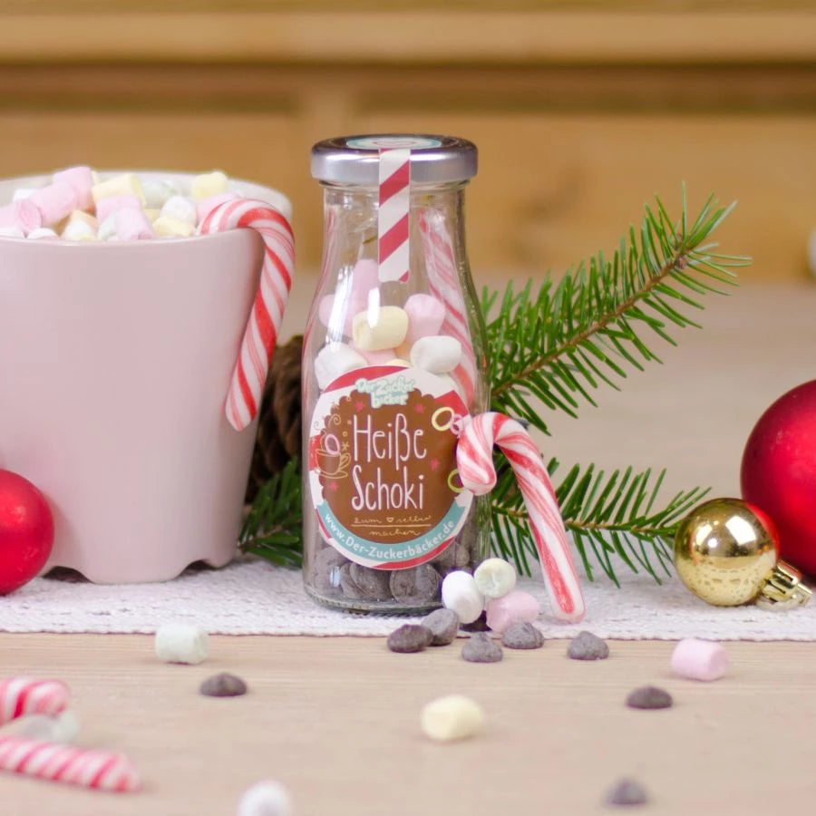 Botella etiquetada "Chocolate caliente" junto a adornos navideños y una taza de malvaviscos.