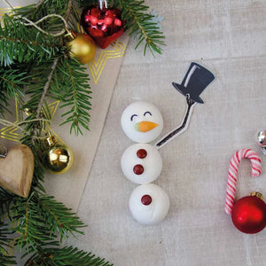 Un muñeco de nieve hecho de malvaviscos con un pan de azúcar, gotas de chocolate y una nariz de zanahoria yace sobre una tela junto a adornos navideños y ramas de abeto.