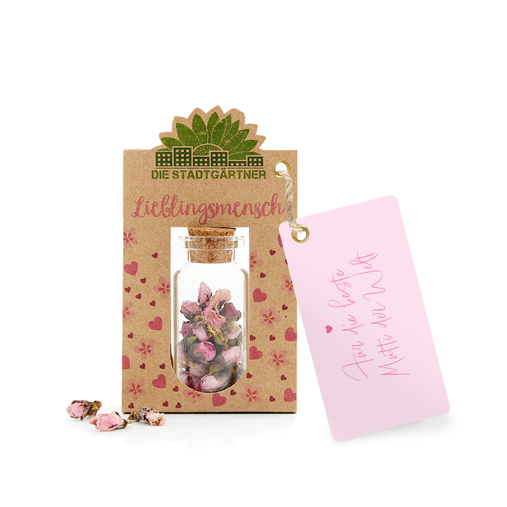 Etiqueta de regalo con la inscripción "Persona Favorita" y una pequeña botella de vidrio con flores secas sobre un fondo de papel kraft junto a una tarjeta rosa con un corazón y "Para Ti".
