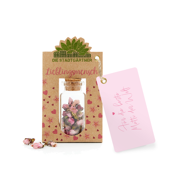 Etiqueta de regalo con la inscripción 'Persona favorita' y una pequeña botella de vidrio con flores secas, junto a ella una tarjeta rosa con el mensaje 'Para ti'.