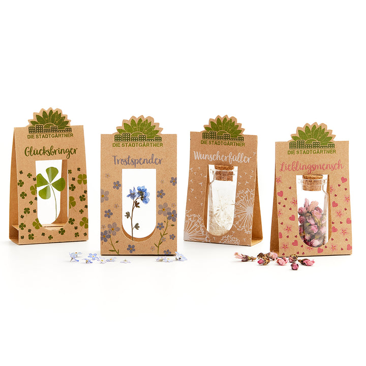 Cuatro cajas de regalo de "Die Stadtgärtner" con pequeños frascos y varias plantas secas, así como etiquetas: Amuleto de la suerte, Consolador, Concededor de deseos y Persona favorita.