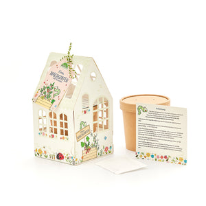Set con un pequeño invernadero decorativo, una maceta, instrucciones y un paquete de semillas para cultivar tomates.