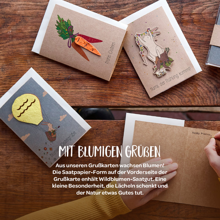 Varias tarjetas de felicitación con motivos decorativos de papel con semillas sobre una mesa de madera, incluidas zanahorias, un conejito y un globo aerostático.