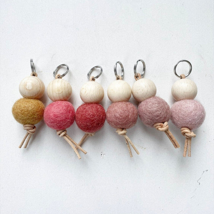 Conjunto de llaveros hechos a mano con bolas de fieltro de lana y cuentas de madera sobre fondo blanco.