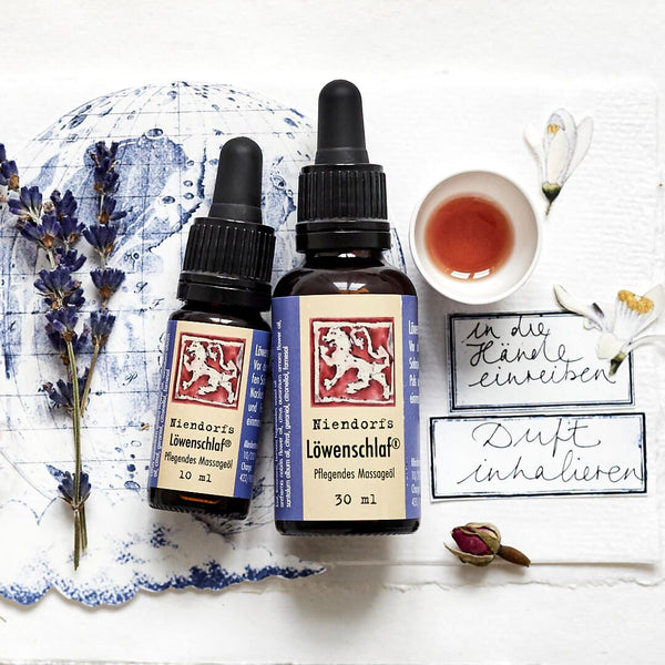 Aceites esenciales sobre un fondo blanco con ramitas de lavanda, una taza de té y notas manuscritas.