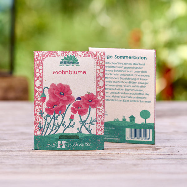 Dos paquetes de semillas de amapola con flores rojas ilustradas sobre un fondo de madera y un jardín borroso como telón de fondo.