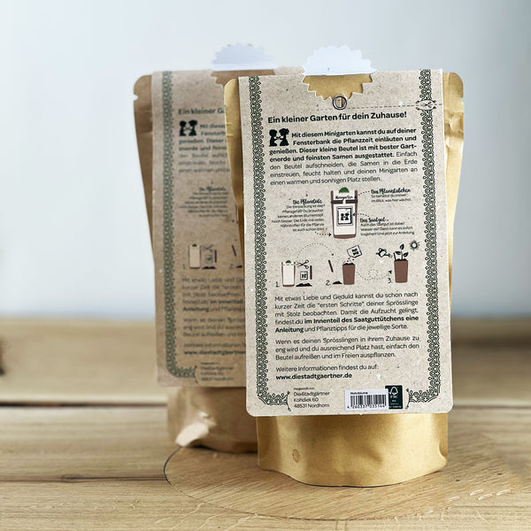 Dos bolsas de papel marrón con instrucciones para un mini jardín en la parte posterior, colocadas sobre una mesa de madera.