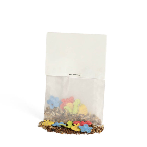 Pequeña bolsa de papel con galletas de colores con forma de flores y animales, algunas de las cuales se han caído, sobre un fondo blanco.