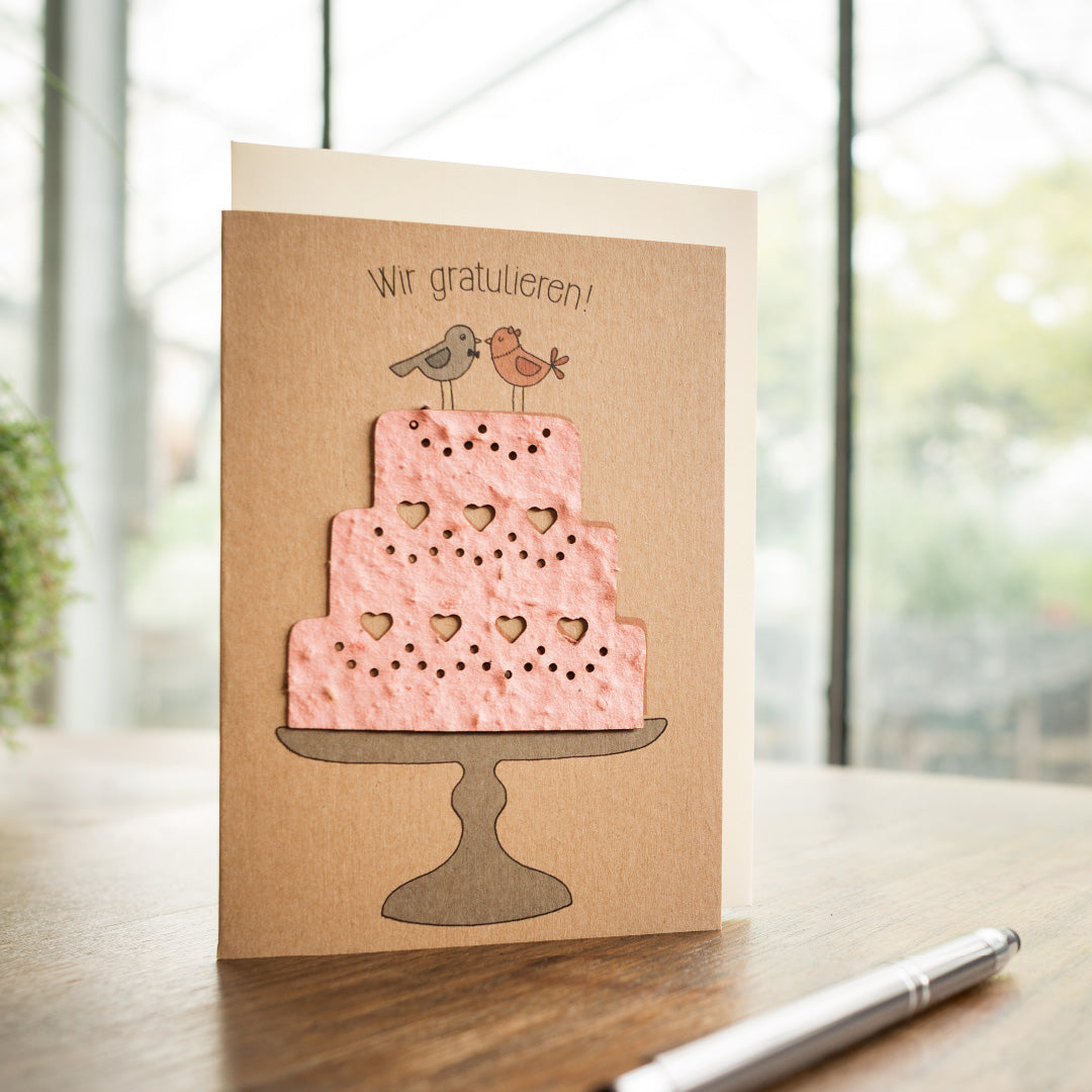Tarjeta de felicitación con un pastel rosa y dos pájaros, con el texto "¡Felicitaciones!" encima.