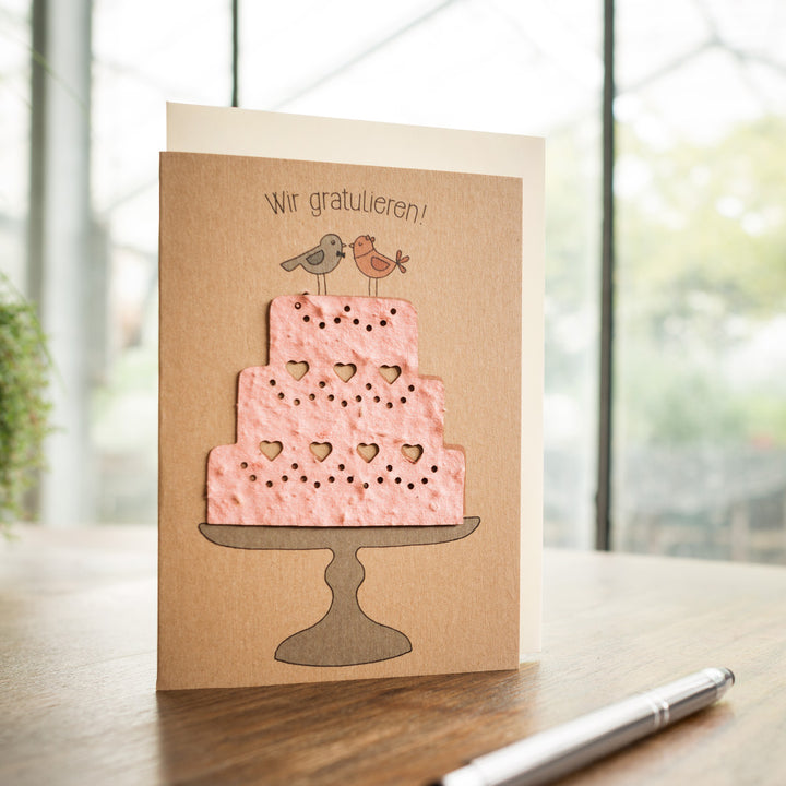 Tarjeta de felicitación con un pastel rosa y dos pájaros, con el texto "¡Felicitaciones!" encima.