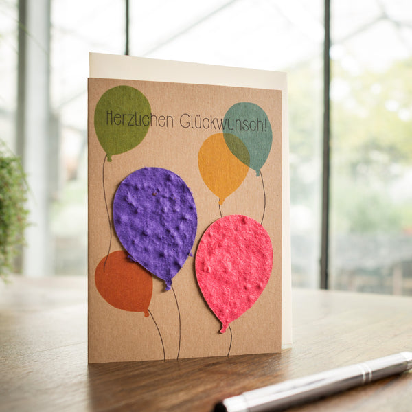Tarjeta de felicitación con globos de colores y las palabras "¡Felicitaciones!" sobre una mesa de madera.