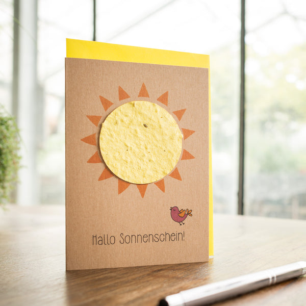 Tarjeta de felicitación hecha a mano con un sol y la inscripción "¡Hola sol!" junto con un pequeño pájaro sobre una mesa de madera.