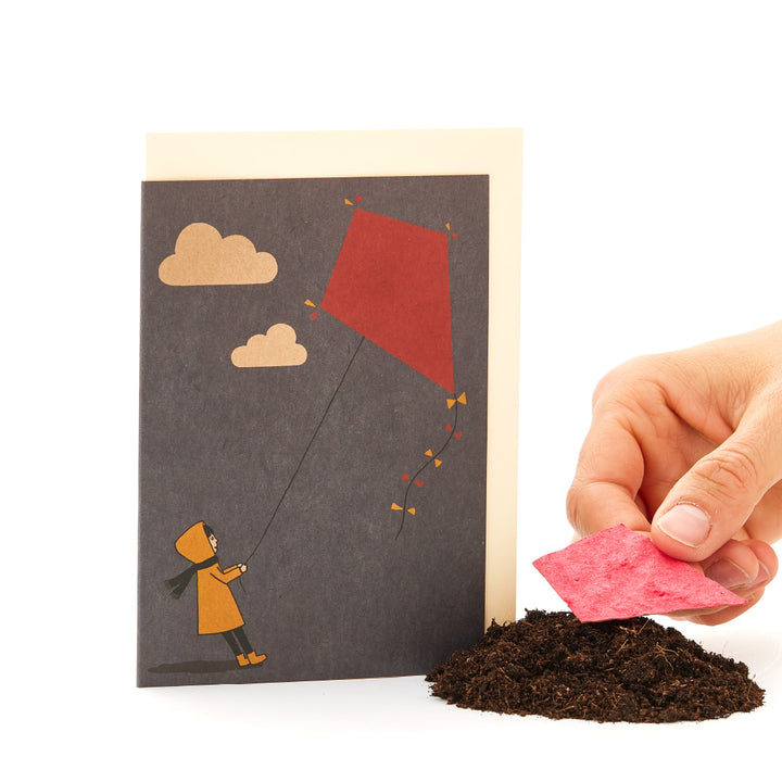 Mano que sostiene una tarjeta de felicitación con la ilustración de un niño volando una cometa.
