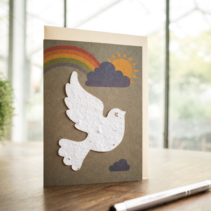 Tarjeta de felicitación con paloma de la paz, arcoíris y sol sobre una mesa.