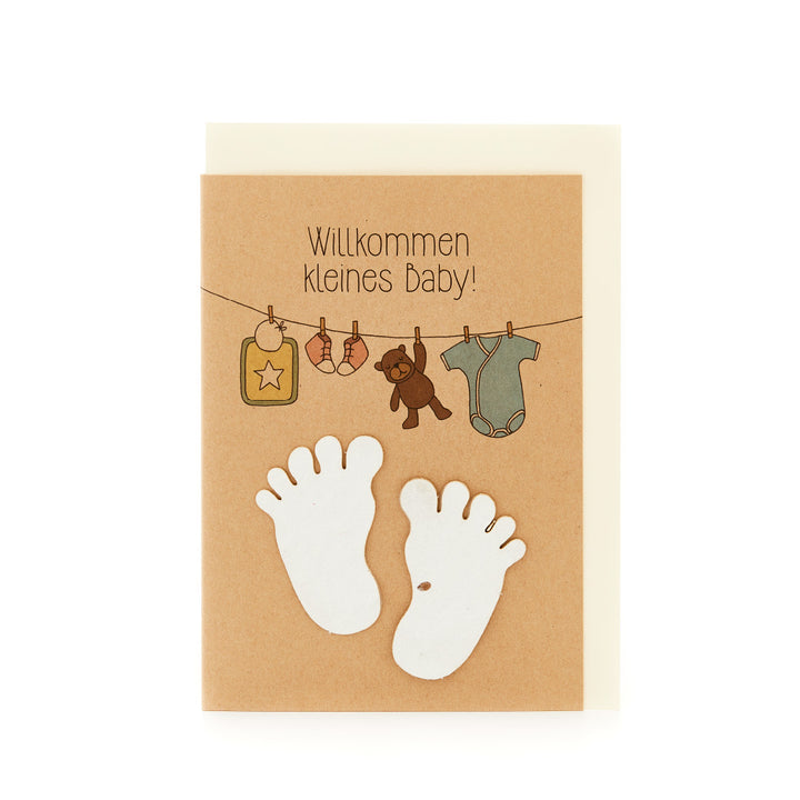 Tarjeta de felicitación de nacimiento con la inscripción "Bienvenido bebé", pies de bebé y ropa de bebé colgada.