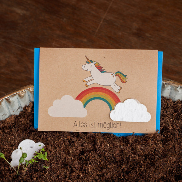 Tarjeta de felicitación con un unicornio y un arcoíris en el suelo, texto "¡Todo es posible!"