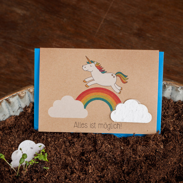 Tarjeta de felicitación con un unicornio y un arcoíris en el suelo, texto "¡Todo es posible!"