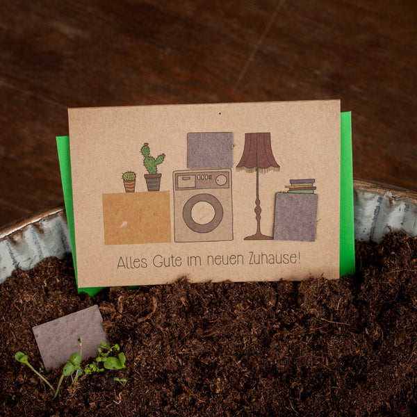Tarjeta de felicitación con plantas en macetas, lavadora y lámpara, texto: ¡Todo lo mejor en tu nuevo hogar!