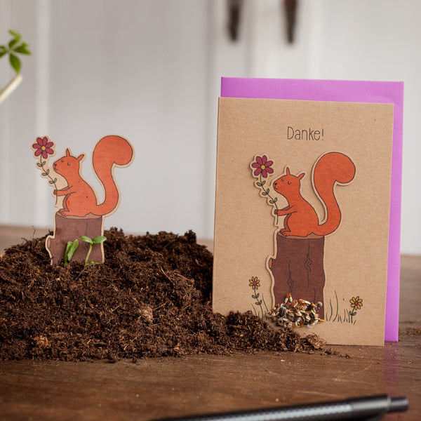 Tarjeta de felicitación con un motivo de ardilla y la palabra "¡Gracias!", junto a una figura de ardilla recortada en la Tierra.