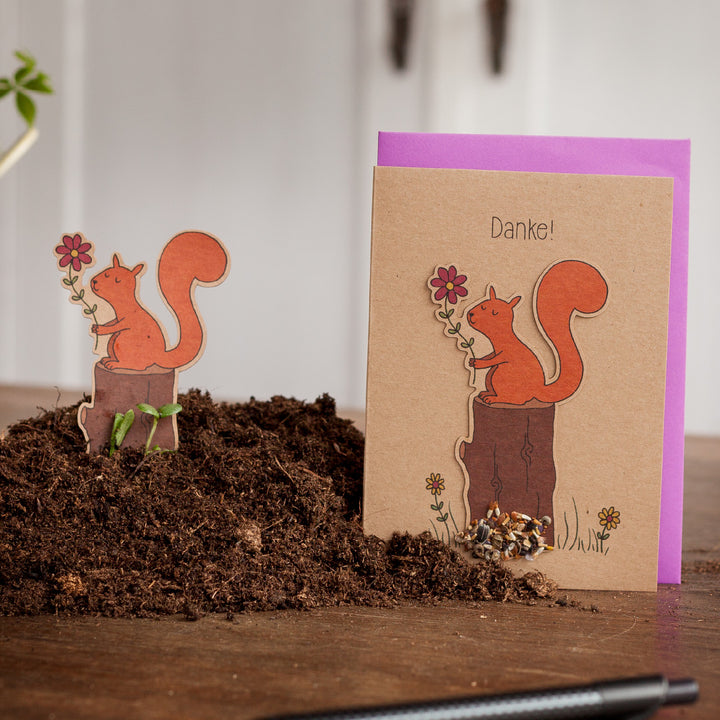 Tarjeta de felicitación con un motivo de ardilla y la palabra "¡Gracias!", junto a una figura de ardilla recortada en la Tierra.