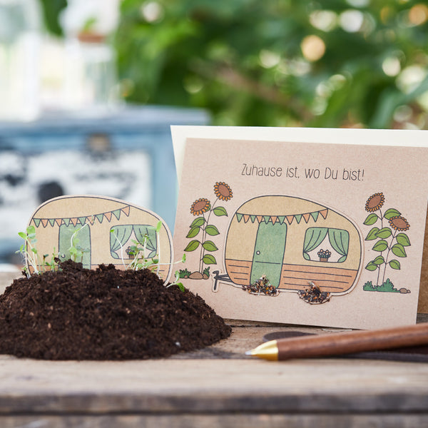 Tarjeta de felicitación dibujada a mano con una autocaravana y flores junto a una pala y tierra.