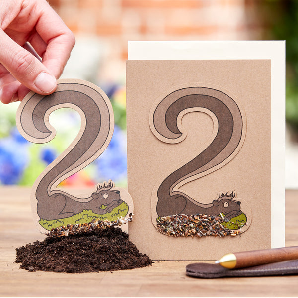Mano sosteniendo una tarjeta de jardín con motivos de ardillas perforados a través de los cuales se ven semillas de pájaros.