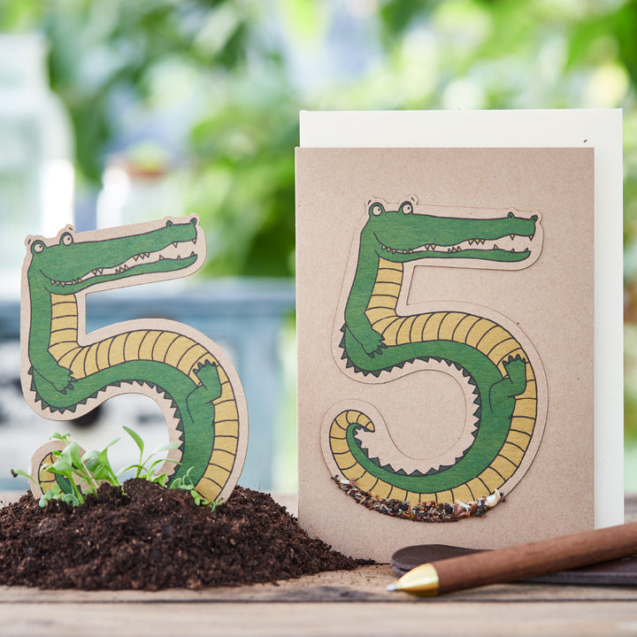 Representación creativa de números como cocodrilos sobre papel, junto a tierra y lápiz.