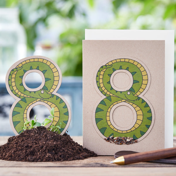 Tarjeta de felicitación creativa con el número 8 diseñado como una serpiente en la tierra con un pequeño bolígrafo al lado.