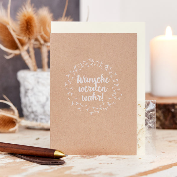 Tarjeta de felicitación con la inscripción "¡Los deseos se hacen realidad!" sobre una mesa junto a una pluma estilográfica y elementos decorativos.