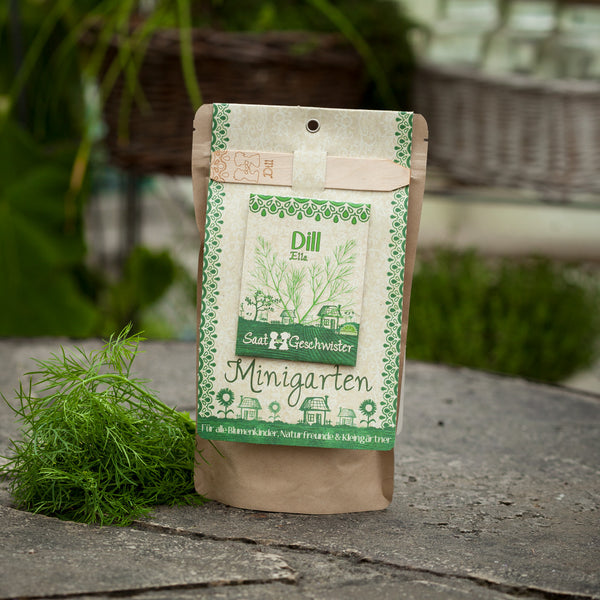 Envase de semillas de eneldo etiquetado “Mini Garden” junto a eneldo fresco sobre una losa de piedra.