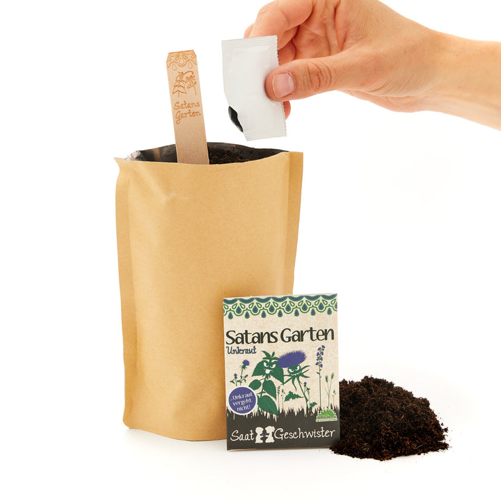 Una mano sosteniendo una bolsa de semillas sobre una bolsa de papel con tierra, junto a un cartel que dice "El jardín de Satanás" y otra bolsa de semillas.