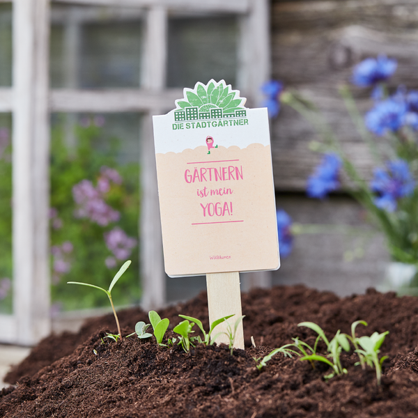 En el jardín hay un cartel que dice "¡La jardinería es mi yoga!" sobre tierra recién plantada.
