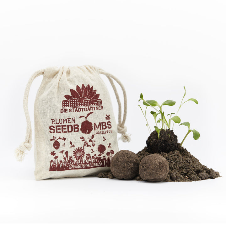 Bolsa de yute con el estampado 'Die Stadtgärtner Blumen Seedbomben', junto a ella plántulas y bolas de tierra sobre un fondo blanco.