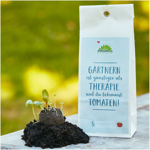 Embalaje del producto "Bombas de semillas" con plantas germinando y el lema "¡La jardinería es más barata que la terapia y obtienes tomates!" sobre un fondo verde difuminado.