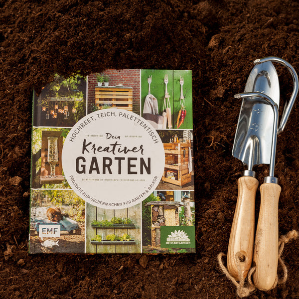 Libro de jardinería titulado "Tu jardín creativo" en el suelo junto a las herramientas de jardinería.