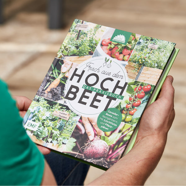 Persona sosteniendo un libro de jardinería titulado "Fresco del cantero elevado" con varias imágenes de jardinería y cosecha.