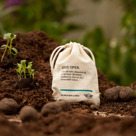 Bolsa de tela con inscripción en el suelo, plantas jóvenes al fondo.