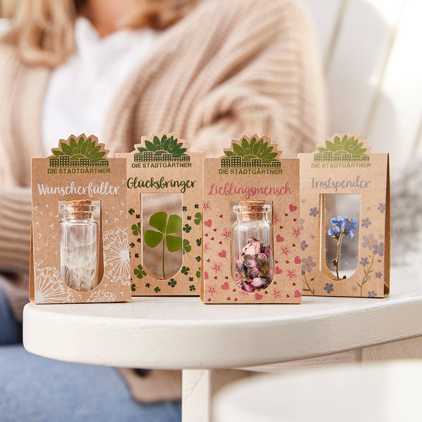 Cuatro pequeños obsequios de "Los Jardineros de la Ciudad" sobre una mesa, con etiquetas como "Relleno de deseos", "Amuleto de la suerte", "Persona favorita" y "Consolador".