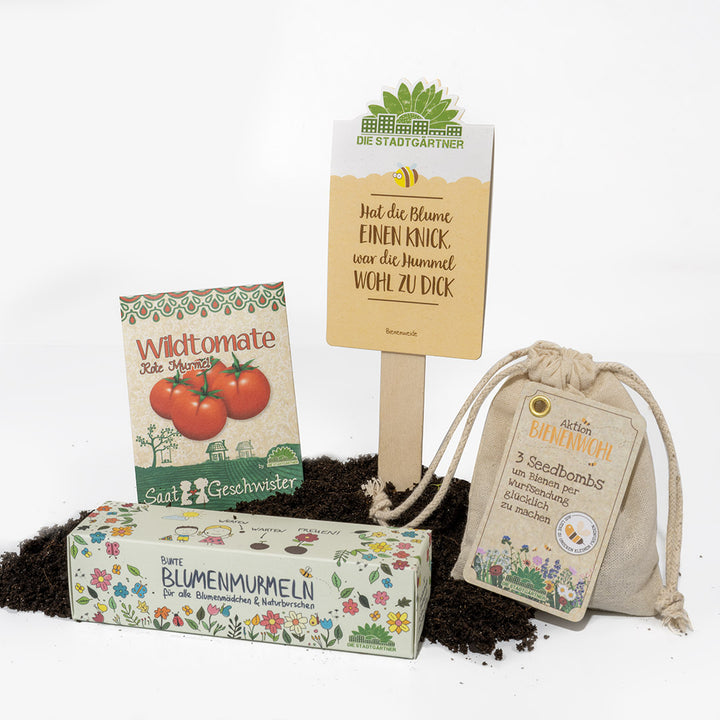 Productos de jardinería en el suelo, incluida una bolsa de semillas de 'tomate silvestre', 'canicas de flores', bolsitas de 'bienestar de las abejas' y un cartel de 'Los jardineros de la ciudad'.