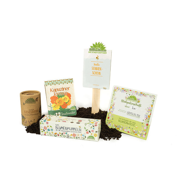 Productos de jardinería que incluyen paquetes de semillas, etiquetas de plantas y macetas biodegradables sobre un fondo blanco.
